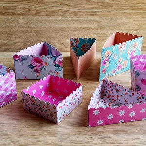 Puede incluir: Un paquete de siete cajas de pastel diferentes en varios patrones florales y geométricos. Las cajas son de cartón y tienen un borde festoneado.