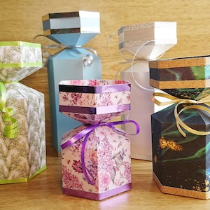 May include: Four decorative gift boxes with different patterns and colors. The boxes are shaped like candy canes and have a ribbon tied around the middle. The patterns include green and white, purple and white, blue and white, and black and green.