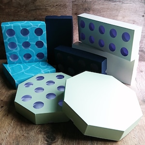 Może przedstawiać: Zestaw pustych pudełek na babeczki w różnych kształtach i rozmiarach. Pudełka są wykonane z tektury i mają jasnozielony, niebieski i biały schemat kolorystyczny. Niektóre pudełka mają wzór z kółek, podczas gdy inne są gładkie.