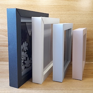 Op de afbeelding: Vier fotolijsten in verschillende maten en kleuren. De grootste lijst is zwart, de volgende is wit, de volgende is lichtblauw en de kleinste is lichtroze.