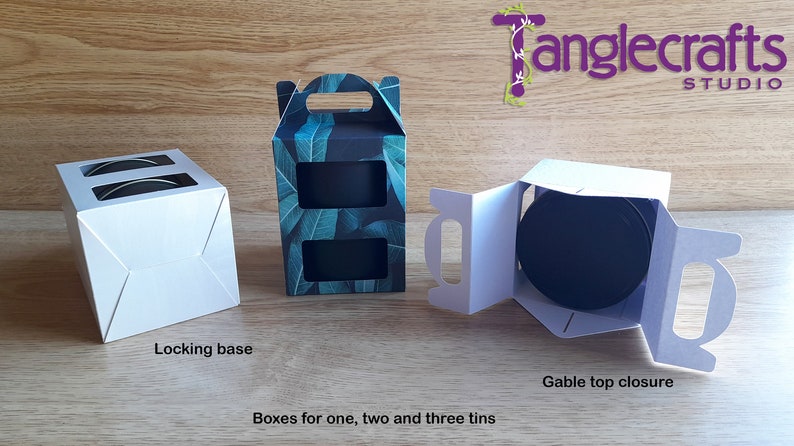 May include: Three white cardboard boxes with different designs for packaging one, two, or three tins. The boxes have a locking base and a gable top closure. The box on the left has a window to show the contents. The box in the middle has a leafy green pattern. The box on the right is open to show the inside.
