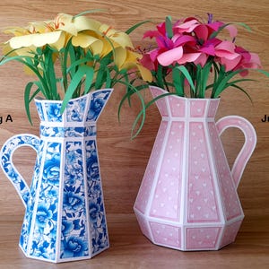 Puede incluir: Dos jarras de cerámica con motivos florales. La jarra etiquetada como "Jug A" es azul y blanca con un diseño floral. La jarra etiquetada como "Jug B" es rosa con un patrón de corazones blancos. Ambas jarras tienen un asa y están llenas de flores de papel.