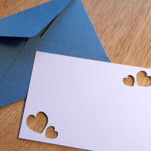 May include: A white card with three heart-shaped cutouts. The card is sitting on top of a blue envelope.