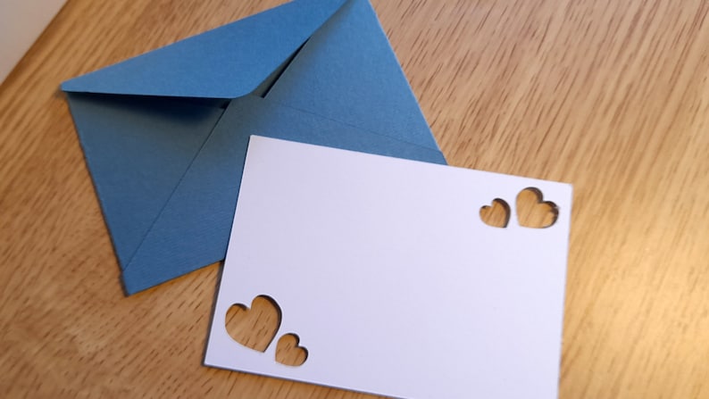 May include: A white card with three heart-shaped cutouts. The card is sitting on top of a blue envelope.