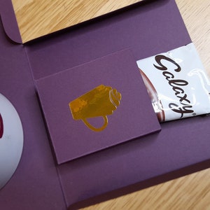 May include: A purple box with a white mug that says "Galaxy" on it. The box also has a chocolate bar and a gold cup icon.