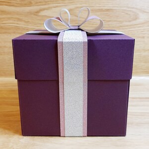 May include: A purple gift box with a white and pink ribbon and bow.