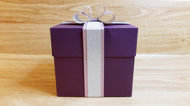 May include: A purple gift box with a white and pink ribbon and bow.
