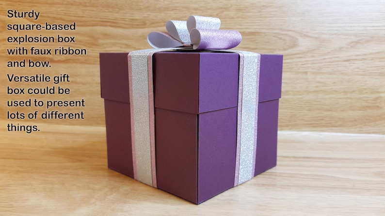 May include: A purple square-based explosion box with a silver and pink ribbon and bow. The box is decorated with silver glitter.  Sturdy square-based explosion box with faux ribbon and bow. Versatile gift box could be used to present lots of different things.