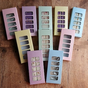 Könnte beinhalten: Sortiment von zehn rechteckigen Boxen mit klaren Fenstern, jede mit sechs Wachs-Schmelzen. Die Boxen sind in verschiedenen Pastellfarben, darunter rosa, lila, blau, grün und gelb.