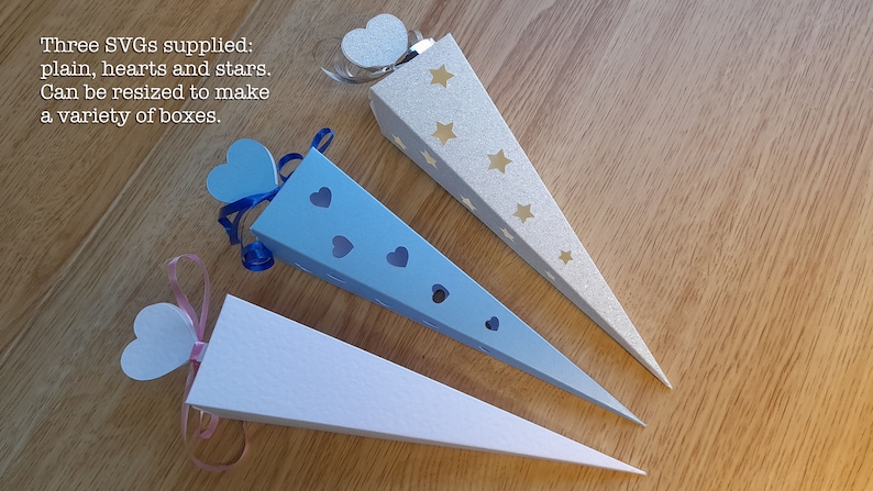 May include: Three paper cones for party favors. One is white, one is light blue with hearts cut out, and one is silver with gold stars. The cones are decorated with ribbons and hearts.