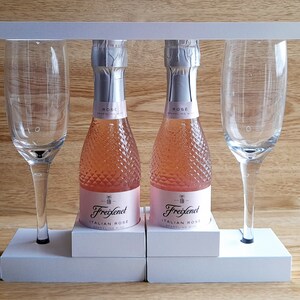May include: Two mini bottles of Freixenet Italian Rose sparkling wine with two champagne flutes on a white wooden stand.
