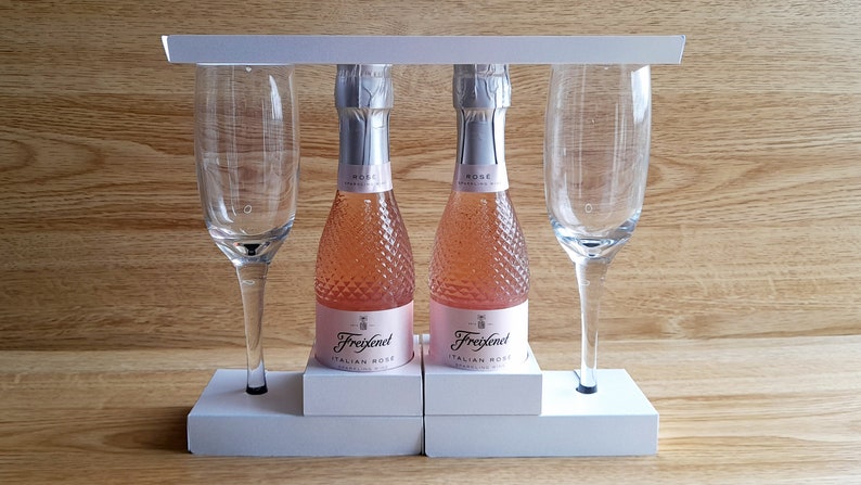 May include: Two mini bottles of Freixenet Italian Rose sparkling wine with two champagne flutes on a white wooden stand.