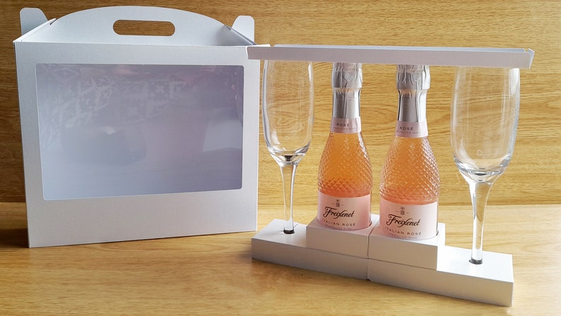 May include: A white gift box with a clear window, containing two small bottles of Freixenet Italian Rose sparkling wine and two champagne flutes.