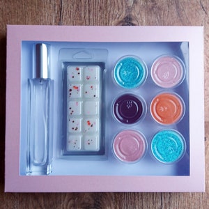 May include: A gift set containing a clear glass bottle of fragrance, a white wax melt with red and orange flecks, and six small containers of colorful glitter.