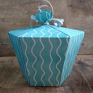 Può includere: Una scatola regalo blu turchese con un motivo ondulato bianco e un fiocco di nastro argentato.