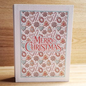 May include: A Christmas greeting card with a festive design. The card features a pattern of gingerbread cookies, candy canes, and hearts. The words "Merry Christmas" are written in red and blue script.