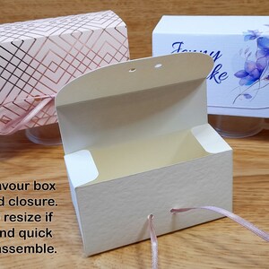 May include: Two favor boxes with ribbon closures. One box is pink with a geometric pattern and the other is white with a floral design. Both boxes are open and have a cream interior.