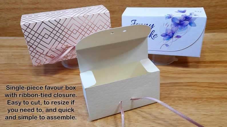May include: Two favor boxes with ribbon closures. One box is pink with a geometric pattern and the other is white with a floral design. Both boxes are open and have a cream interior.