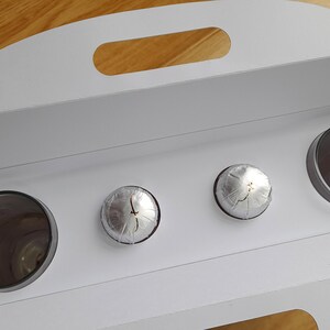 May include: A white cardboard box with a handle, open to reveal three silver-wrapped items and a clear glass container.