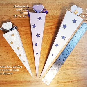 May include: Three cone-shaped paper party favor boxes with star cutouts. The boxes are made from white, light purple, and silver cardstock. The boxes are 12 inches by 12 inches, and the largest box is cut from a sheet of A3 paper. The smaller boxes are cut from A4 paper. The text "Cut from A4, at the size it comes into Design Space" is written below the silver box. The text "Enlarged and out from 12" x 12" is written above the light purple box. The text "Cut as large as possible from a sheet of A3" is written above the white box.