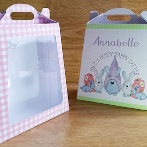 以下が含まれることがあります： ピンクと白のギンガムチェック柄の箱と、緑と白のギンガムチェック柄の箱の2つのイースターギフトボックス。緑の箱には「Annabelle Have a Hoppy Happy Easter」の文字が書かれています。