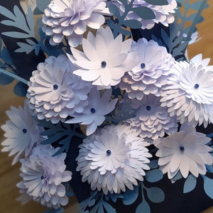 May include: A bouquet of paper flowers in shades of blue and white. The flowers are made of paper and have a 3D effect. The flowers are arranged in a vase and are surrounded by green leaves.