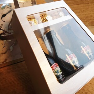 Pode incluir: Uma caixa de presente branca com uma janela transparente, contendo tr&ecirc;s garrafas em miniatura de Baileys Irish Cream e algumas trufas de chocolate. A caixa est&aacute; sobre uma superf&iacute;cie de madeira.