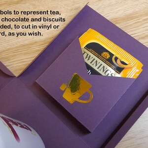 May include: A purple box with four pockets, each with a gold symbol representing tea, coffee, hot chocolate, and biscuits. The box includes a tea bag in a yellow envelope with the text "TWININGS" printed on it.