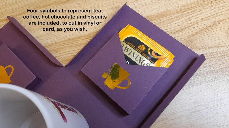 May include: A purple box with four pockets, each with a gold symbol representing tea, coffee, hot chocolate, and biscuits. The box includes a tea bag in a yellow envelope with the text "TWININGS" printed on it.