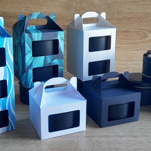May include: Assortment of black candle tins with lids, packaged in various cardboard boxes with cut-out windows and handles. The boxes have different patterns, including blue waves, green leaves, and solid white and black.