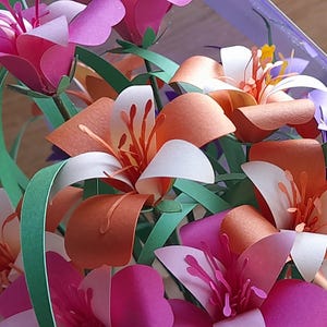 May include: A bouquet of paper flowers in shades of pink, orange, and white. The flowers are made of paper and have a realistic appearance. The bouquet is arranged in a clear vase.