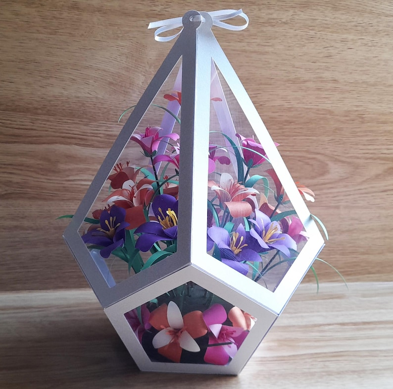 May include: A white geometric paper flower vase with a variety of colorful paper flowers inside. The vase is shaped like a diamond and has a hexagonal base.
