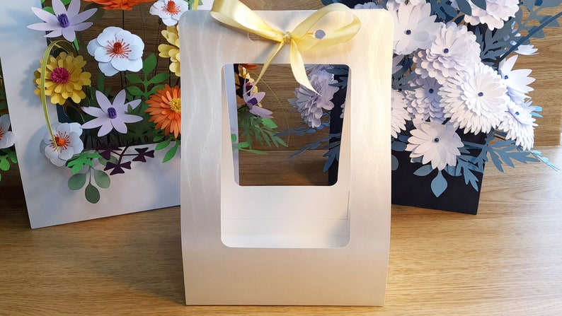 May include: A white paper gift box with a window and a yellow ribbon. The box is empty and has a white background.
