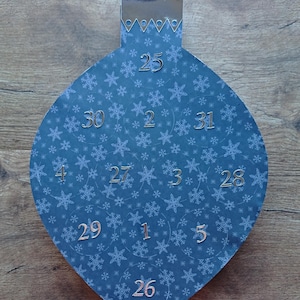 May include: A blue Christmas ornament with a snowflake pattern and silver numbers from 1 to 31.