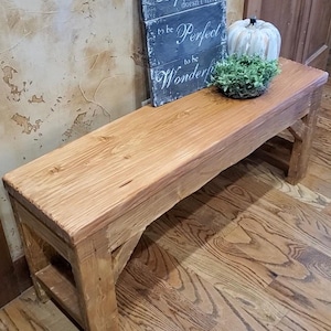May include: A rectangular wooden bench with a natural light brown finish and visible wood grain. The bench features sturdy legs with angled support braces. A dark gray sign with white text reading Life doesn't have to be Perfect to be Wonderful.