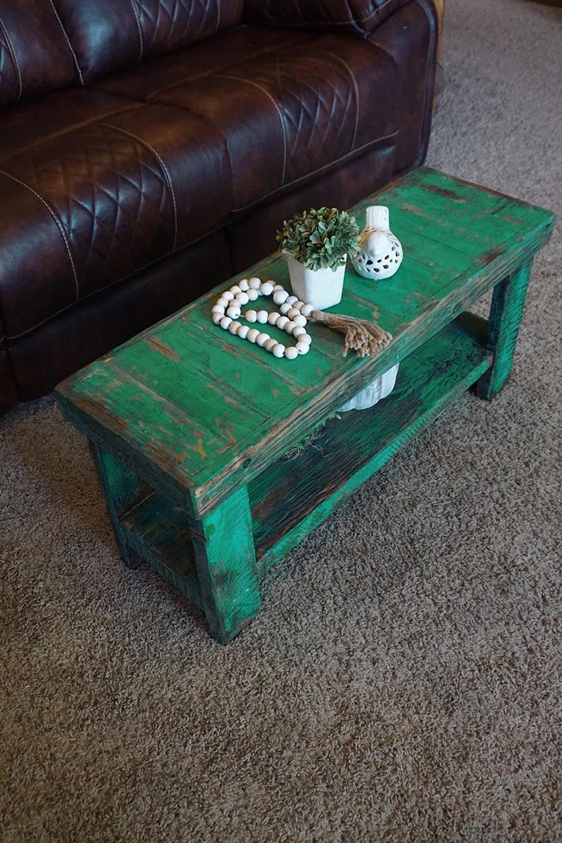 May include: A distressed, rectangular coffee table painted in a vibrant green. The table features a lower shelf and is accessorized with a white beaded garland, a small potted plant, and a decorative white ceramic piece. The table is made of wood.