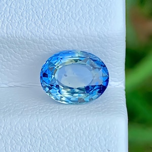 Op de afbeelding: Een ovaal geslepen edelsteen met een levendige blauwe kleur en een gefacetteerd oppervlak. De steen vertoont een heldere, transparante kwaliteit waarbij het licht reflecteert op de vele geometrische facetten voor een schittering.