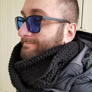 May include: A black knitted infinity scarf and black-framed sunglasses with blue lenses. The scarf is thick and textured. The sunglasses have a classic square shape.