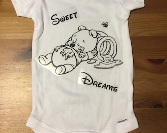 May include: White baby onesie with a black and white Winnie the Pooh design. The design shows Winnie the Pooh sleeping next to a honey pot with the words "Sweet Dreams".