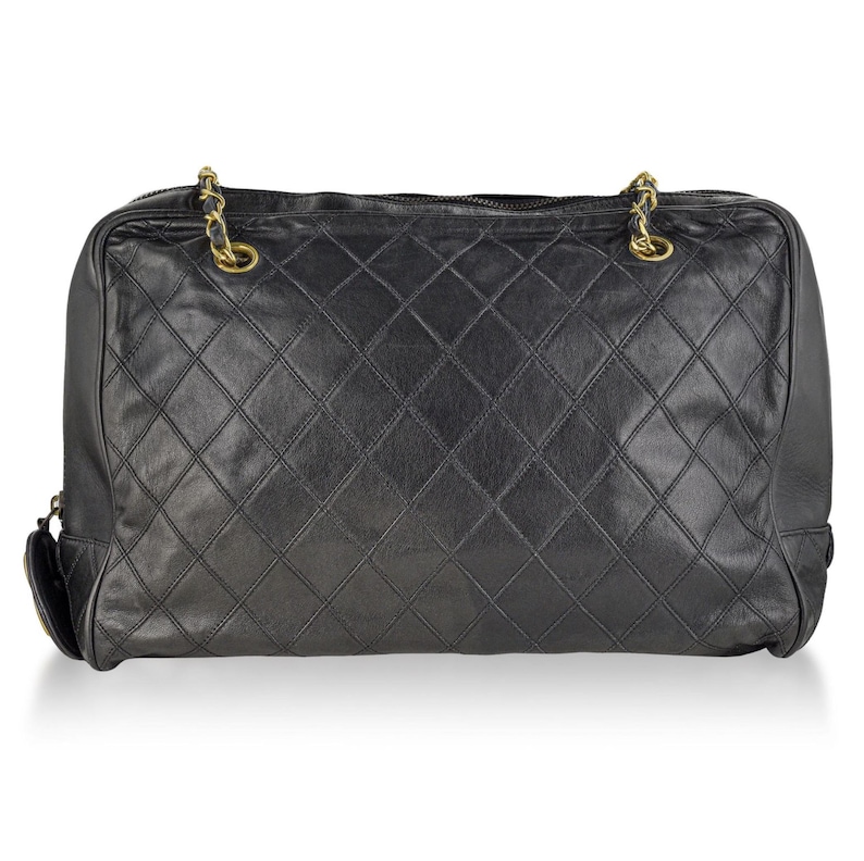 May include: Black quilted leather handbag with gold-tone chain straps. The rectangular bag features a diamond pattern and a top zipper closure. The bag has a classic, timeless design.