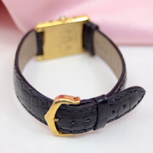 May include: A gold wristwatch with a black leather band. The band has a crocodile pattern and a gold buckle.