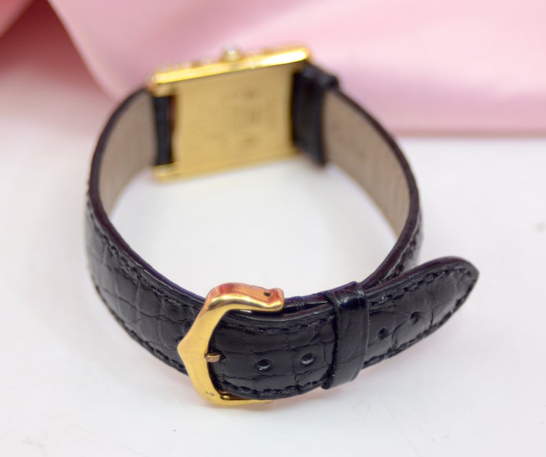 May include: A gold wristwatch with a black leather band. The band has a crocodile pattern and a gold buckle.
