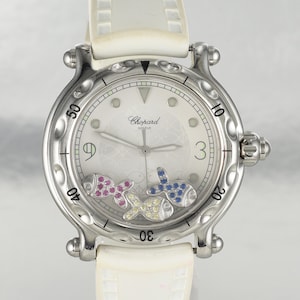May include: A luxury wristwatch with a white dial and a stainless steel case. The watch features three colorful fish-shaped charms and a white leather strap. The dial displays the Chopard Geneve logo and the numbers 3, 9, 10, 20, 30, 40, and 50.