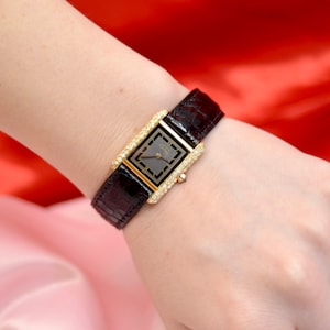 May include: A gold watch with a black face and diamond bezel. The watch has a black leather band.