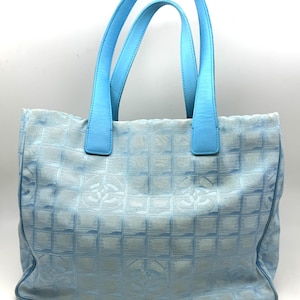 Puede incluir: Un bolso tote azul claro con asas azules a juego. El bolso presenta un patr&oacute;n de cuadr&iacute;cula con logotipos repetidos. Las asas son de un tono azul m&aacute;s claro que el cuerpo del bolso.