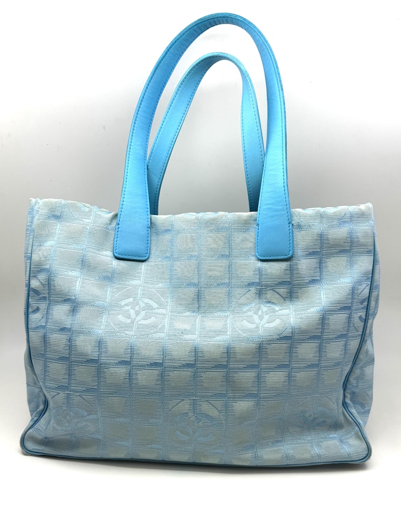 Puede incluir: Un bolso tote azul claro con asas azules a juego. El bolso presenta un patr&oacute;n de cuadr&iacute;cula con logotipos repetidos. Las asas son de un tono azul m&aacute;s claro que el cuerpo del bolso.