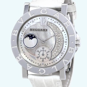 May include: A silver Bulgari watch with a white leather band. The watch face is white with a moon phase complication and a diamond-encrusted bezel.