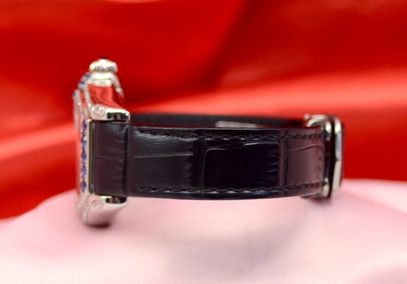 May include: A silver wristwatch with a black leather band. The watch face is surrounded by small blue gemstones.