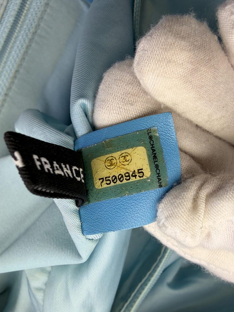 Puede incluir: Primer plano de una tela azul claro con una etiqueta negra que dice "FRANCE" y una etiqueta azul con el n&uacute;mero "7500945". Las etiquetas est&aacute;n adheridas a la tela.