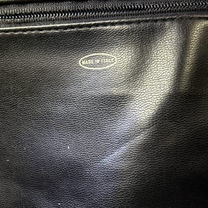 May include: Close-up of a black leather item with a zipper and the text "MADE IN ITALY" in a white oval. The leather has a textured surface.